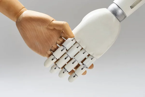 Robot y muñeca de madera estrechando las manos aislados en gris - foto de stock