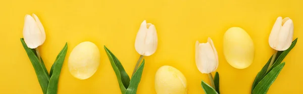Top view of tulips and painted Easter eggs on colorful yellow background, panoramic shot — Stock Photo