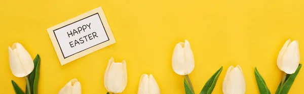 Top view of tulips, greeting card with happy Easter lettering on yellow colorful background, panoramic shot — Stock Photo