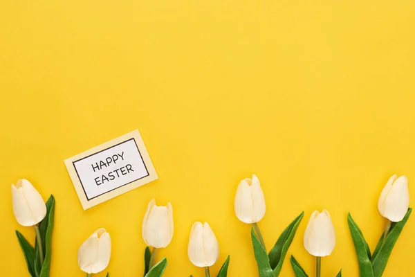 Top view of tulips, greeting card with happy Easter lettering on yellow colorful background — Stock Photo