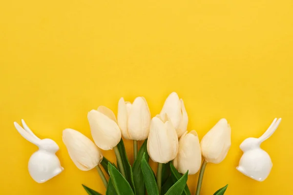 Top view of tulips and white Easter bunnies on colorful yellow background — Stock Photo