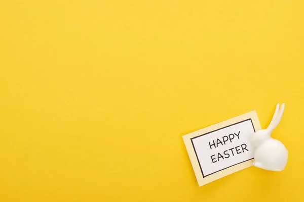 Top view of greeting card with happy Easter lettering near Easter white bunny on yellow colorful background — Stock Photo