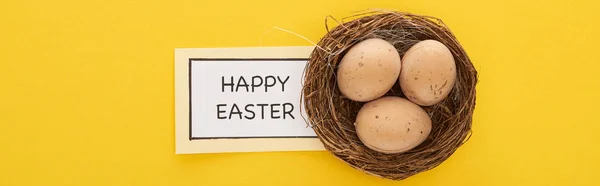 Top view of greeting card with happy Easter lettering near chicken eggs in nest on yellow colorful background, panoramic shot — Stock Photo