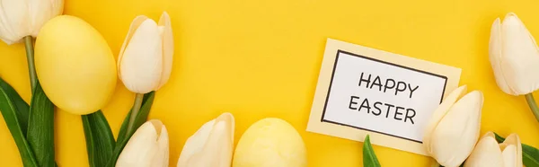 Draufsicht auf Tulpen und bemalte Ostereier in Kartennähe mit fröhlichem Osteraufdruck auf buntem gelben Hintergrund, Panoramaaufnahme — Stockfoto
