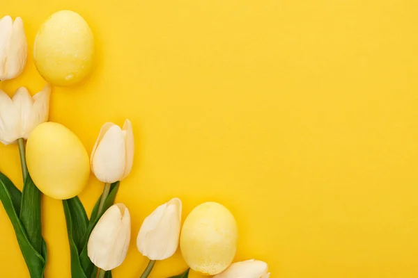 Vue de dessus des tulipes et des œufs de Pâques peints sur fond jaune coloré — Photo de stock