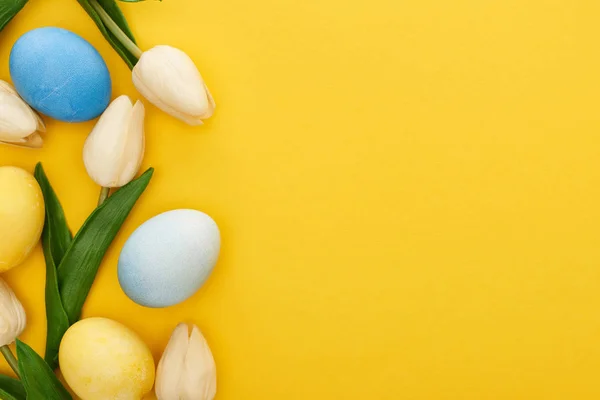 Vista superior de tulipas e ovos de Páscoa pintados sobre fundo amarelo colorido com espaço de cópia — Fotografia de Stock