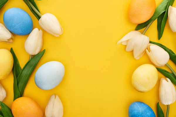 Vista superior de tulipas e ovos de Páscoa pintados sobre fundo amarelo colorido com espaço de cópia — Fotografia de Stock