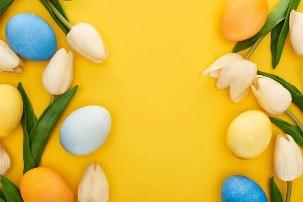 Vista superior de tulipas e ovos de Páscoa pintados sobre fundo amarelo colorido com espaço de cópia — Stock Photo