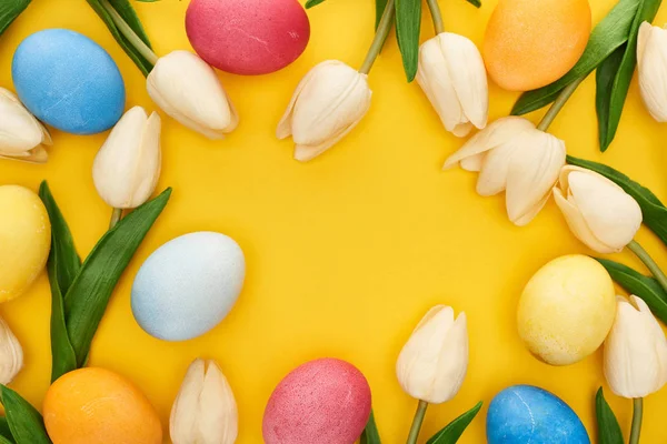 Верхний вид тюльпанов и окрашенных пасхальных яиц на красочном желтом фоне с копировальным пространством — стоковое фото
