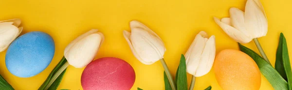 Top view of tulips and painted Easter eggs on colorful yellow background, panoramic shot — Stock Photo