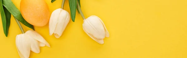 Top view of tulips and painted Easter egg on colorful yellow background, panoramic shot — Stock Photo