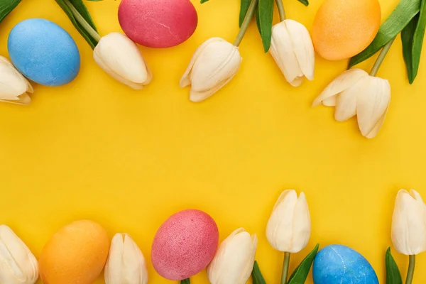 Vista superior de tulipas e ovos de Páscoa pintados sobre fundo amarelo colorido com espaço de cópia — Fotografia de Stock