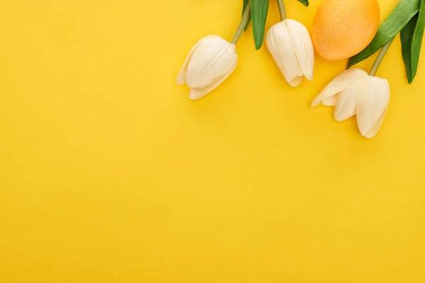 Vista superior de tulipas e ovo de Páscoa pintado sobre fundo amarelo colorido — Fotografia de Stock