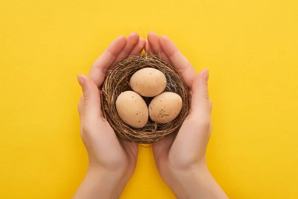 Vue recadrée de la femme tenant des œufs de poulet dans le nid sur fond jaune coloré — Photo de stock