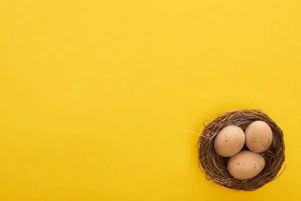 Vista superior de huevos de pollo en el nido sobre fondo amarillo colorido con espacio de copia - foto de stock