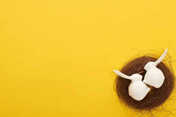 Von oben Ansicht der weißen Osterhasen Figuren im Nest auf bunten gelben Hintergrund mit Kopierraum — Stock Photo