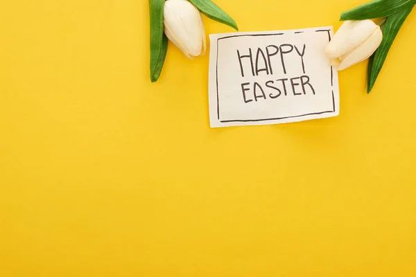 Draufsicht auf Grußkarte mit fröhlichem Osteraufdruck und Tulpen auf gelbem, buntem Hintergrund — Stockfoto