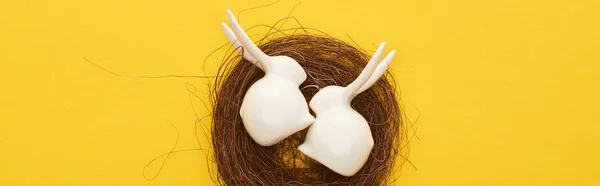 Top view of white Easter bunnies figurines in nest on colorful yellow background, panoramic shot — Stock Photo