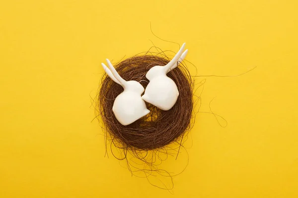Top view of white Easter bunnies figurines in nest on colorful yellow background — Stock Photo