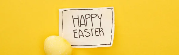 Вид зверху вітальні листівки з щасливим Великоднім листям і розмальованим яйцем на жовтому барвистому фоні, панорамний знімок — стокове фото