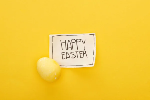 Top view of greeting card with happy Easter lettering and painted egg on yellow colorful background — Stock Photo