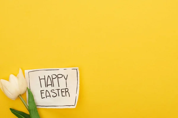 Vista superior de tulipán y tarjeta de felicitación con letras de Pascua feliz sobre fondo amarillo colorido - foto de stock