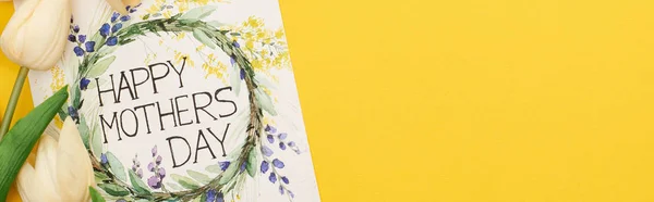 Top view of spring tulips and happy mothers day greeting card on colorful yellow background, panoramic shot — Stock Photo