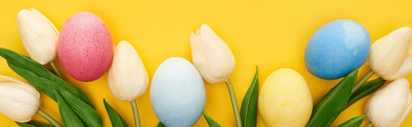 Top view of tulips and painted Easter eggs on colorful yellow background, panoramic shot — Stock Photo