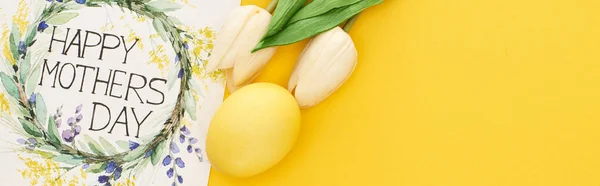 Vista superior de los tulipanes de primavera, huevo de Pascua y feliz tarjeta de felicitación del día de las madres sobre el fondo amarillo colorido, tiro panorámico - foto de stock