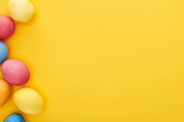 Top view of multicolored painted Easter eggs on yellow background with copy space — Stock Photo