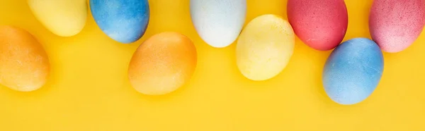 Top view of multicolored painted Easter eggs on yellow background, panoramic shot — Stock Photo