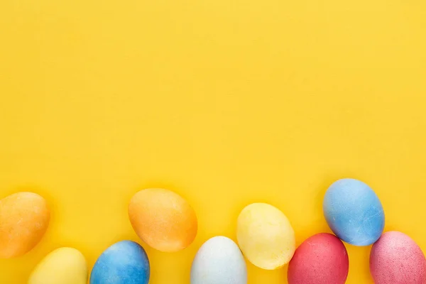Top view of multicolored painted Easter eggs on yellow background with copy space — Stock Photo