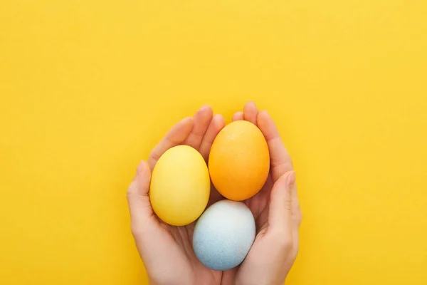 Vista recortada de la mujer sosteniendo huevos de Pascua pintados multicolores sobre fondo amarillo - foto de stock