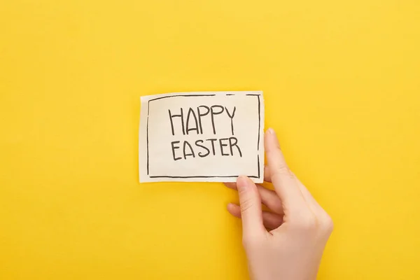 Vista recortada de la mujer que sostiene la tarjeta de felicitación con letras de Pascua feliz sobre fondo amarillo - foto de stock