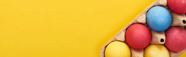 Vista superior de ovos de Páscoa pintados multicoloridos em recipiente de papelão no fundo amarelo com espaço de cópia, tiro panorâmico — Fotografia de Stock