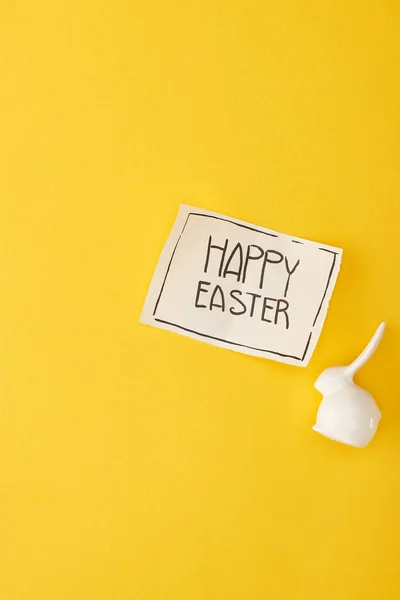 Top view of decorative bunny and greeting card with happy Easter lettering on yellow colorful background — Stock Photo