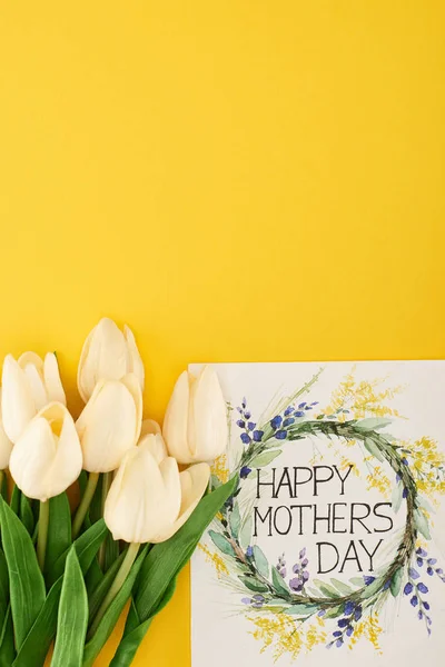 Vista superior de los tulipanes de primavera y feliz tarjeta de felicitación del día de las madres sobre el fondo amarillo colorido - foto de stock