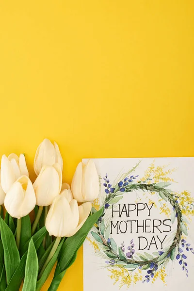 Top view of spring tulips and happy mothers day greeting card on colorful yellow background — Stock Photo
