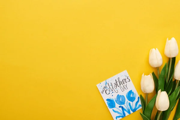 Vista superior de los tulipanes de primavera y feliz tarjeta de felicitación del día de las madres sobre el fondo amarillo colorido - foto de stock