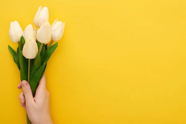 Vue recadrée de la femme tenant des tulipes de printemps sur fond jaune coloré — Photo de stock