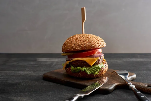 Leckere Frischfleisch-Cheeseburger auf Holzbrett in der Nähe von Besteck — Stockfoto