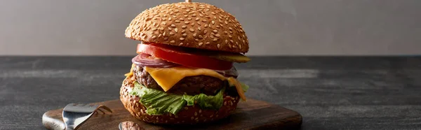Köstlicher Frischfleisch-Cheeseburger auf Holzbrett in der Nähe von Besteck, Panoramaaufnahme — Stockfoto