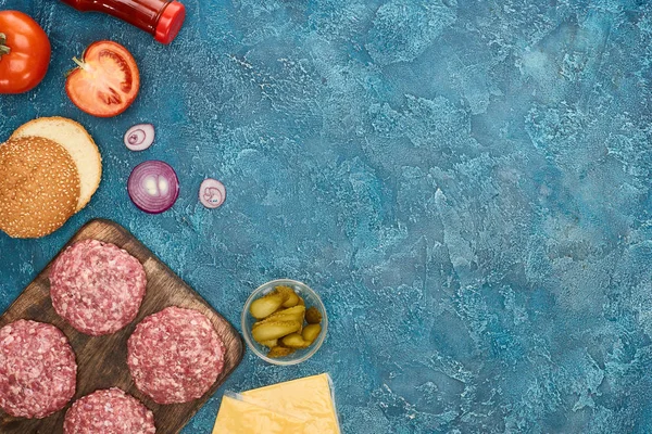Вид зверху свіжих інгредієнтів бургерів на синій текстурованій поверхні з простором для копіювання — стокове фото