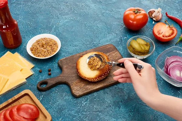 Vista ritagliata della donna che aggiunge senape sul panino sulla superficie strutturata blu — Foto stock