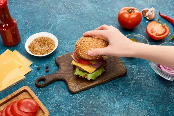 Teilansicht einer Frau, die köstlichen Burger auf blau strukturierter Oberfläche kocht — Stockfoto