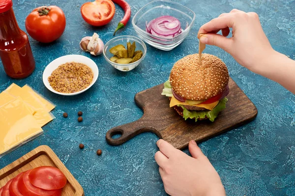 Partial view of woman cooking delicious burger on blue textured surface — Stock Photo