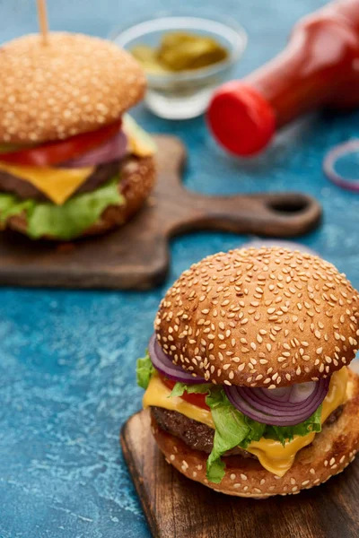 Foco seletivo de delicioso cheeseburger na placa de madeira na superfície texturizada azul — Fotografia de Stock