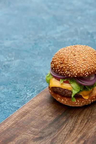 Deliciosa hamburguesa con queso sobre tabla de madera sobre superficie de textura azul - foto de stock