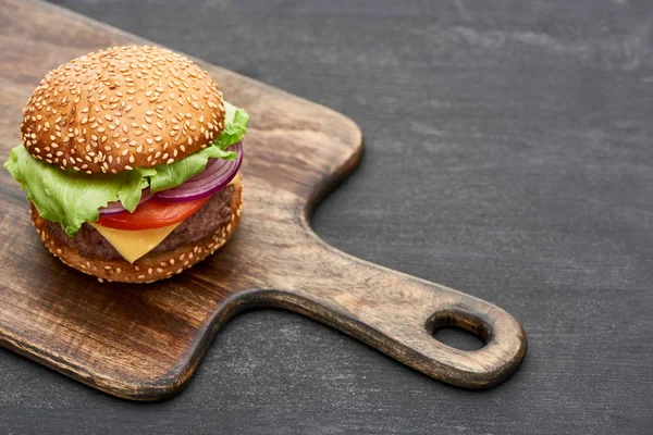 Delicious fresh cheeseburger on wooden board on grey surface — Stock Photo