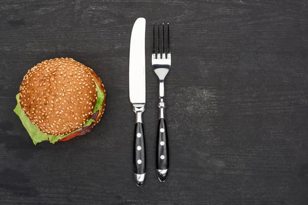 Top view of delicious fresh burger on black wooden table with knife and fork — Stock Photo